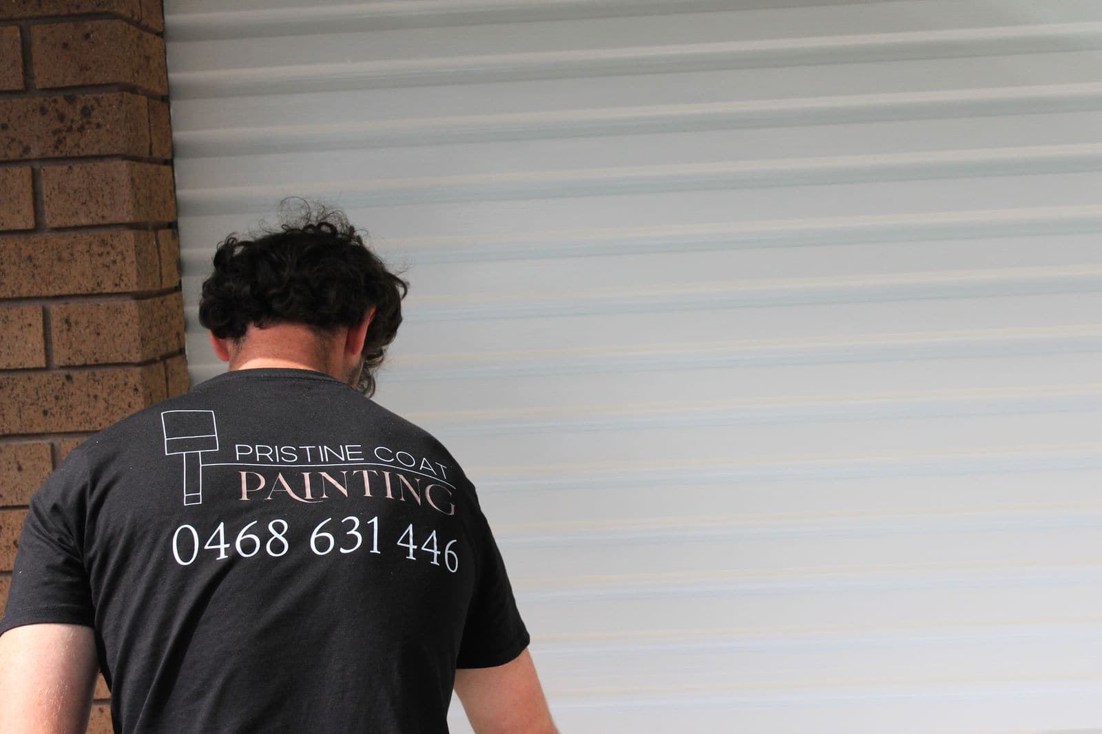 A painter in a Pristine Coat Painting work shirt printed with the business phone number