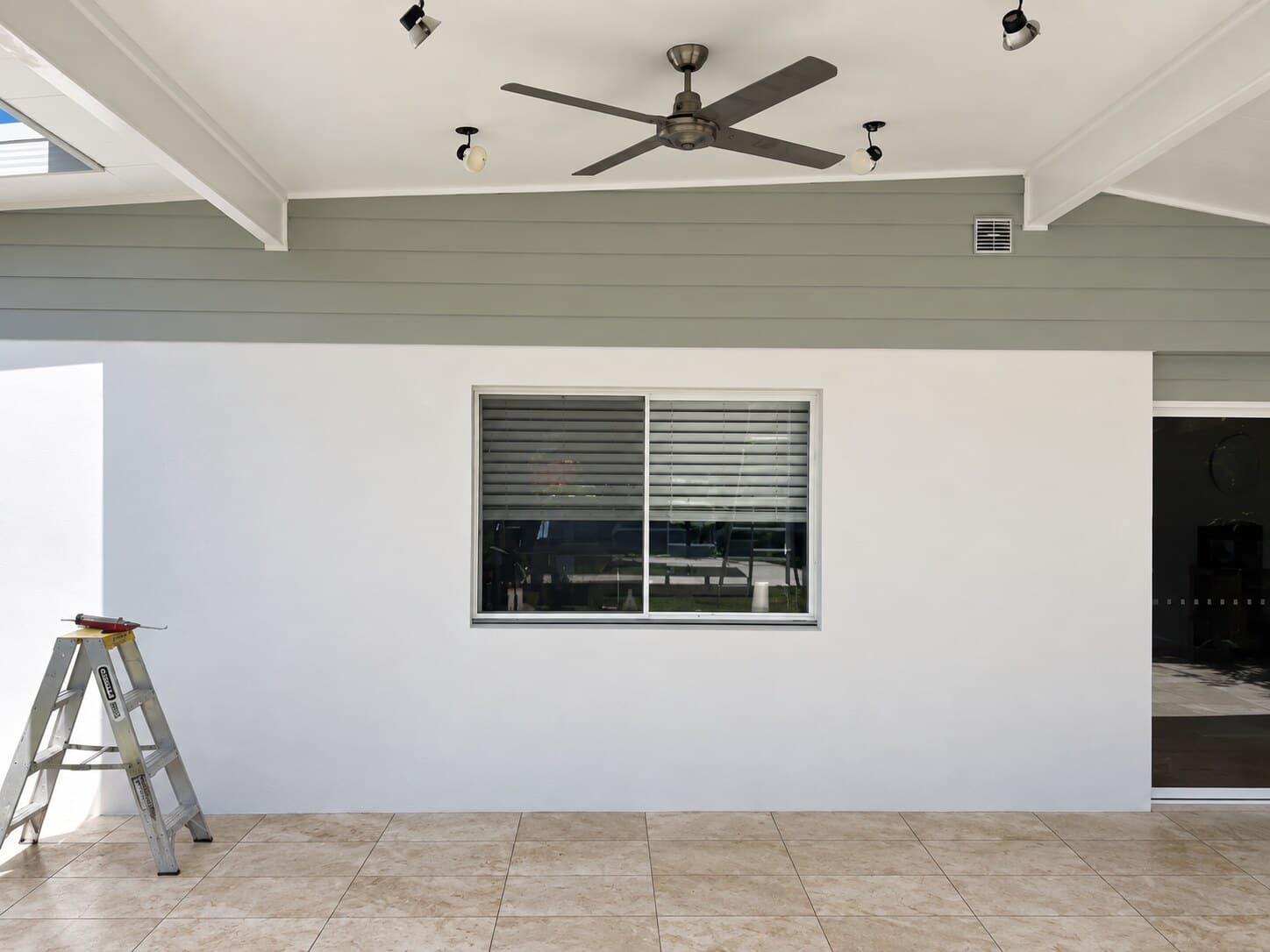 Covered outdoor area with white walls, grey-green weatherboards and a painter's ladder