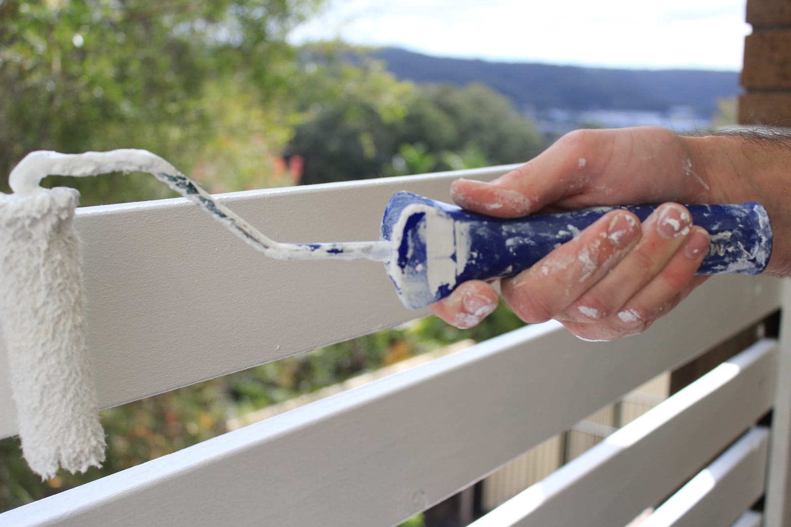 Close-up of a painter rolling white paint onto a balustrade